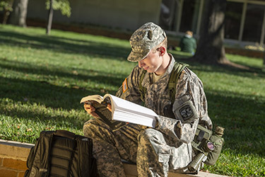 photo of a student reading a book outside on campus