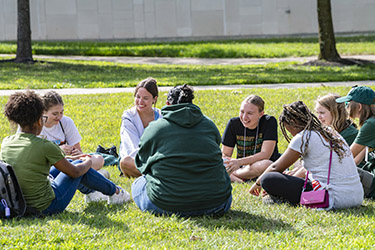 photo of students sitting in a circle on the grass on campus