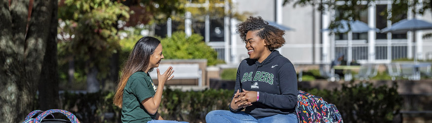 photo of two students sitting outside on campus and signing