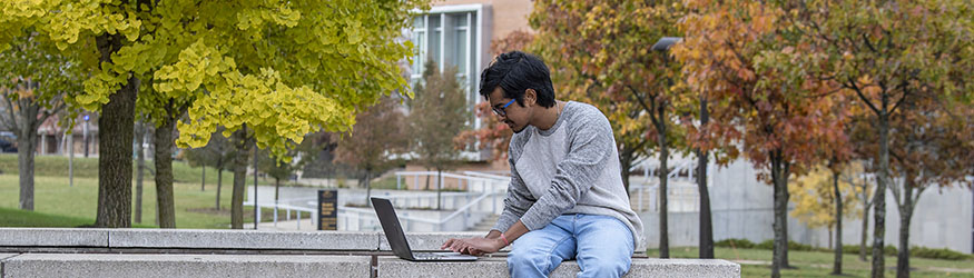 photo of a student with a laptop sitting outside on campus